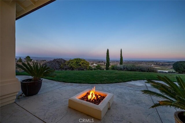 patio terrace at dusk featuring a fire pit and a yard