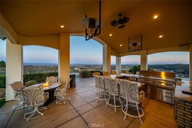 patio terrace at dusk featuring an outdoor fire pit, grilling area, and exterior kitchen