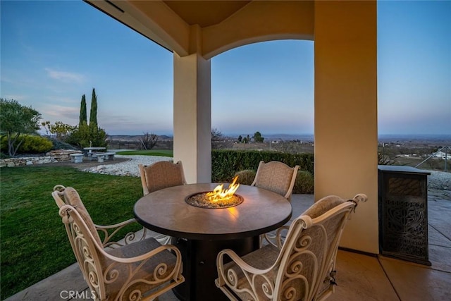 patio terrace at dusk with a fire pit, a yard, and a water view