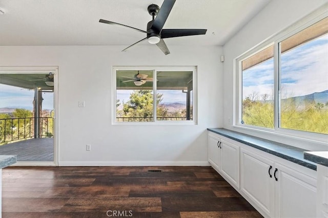 empty room featuring a healthy amount of sunlight, dark wood-type flooring, and ceiling fan