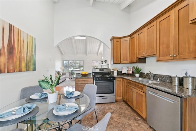 kitchen featuring appliances with stainless steel finishes, beamed ceiling, sink, dark stone counters, and kitchen peninsula