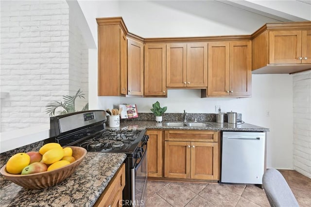 kitchen featuring dark stone countertops, sink, brick wall, and appliances with stainless steel finishes