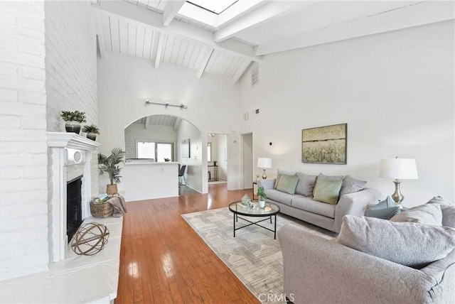 living room featuring lofted ceiling with beams, a brick fireplace, and light wood-type flooring