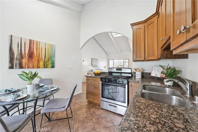 kitchen featuring tile patterned floors, lofted ceiling, sink, stainless steel gas stove, and dark stone counters