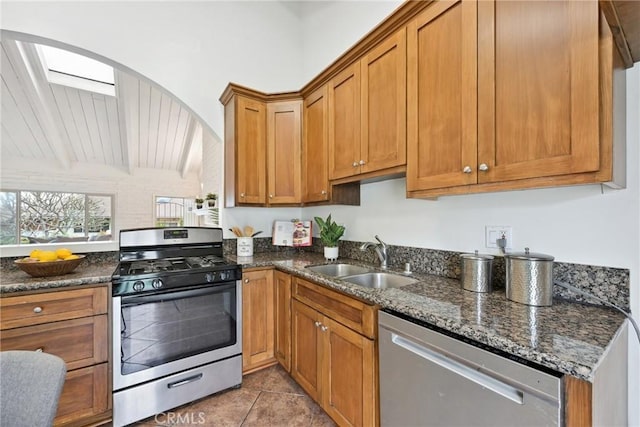 kitchen with dark stone countertops, sink, stainless steel appliances, and vaulted ceiling with skylight