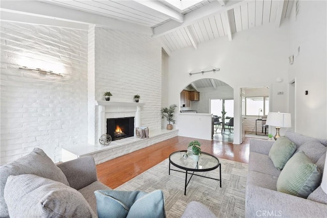 living room with high vaulted ceiling, light hardwood / wood-style floors, beamed ceiling, and brick wall