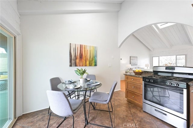 kitchen featuring vaulted ceiling with beams, stainless steel range with gas stovetop, dark stone counters, and dark tile patterned flooring