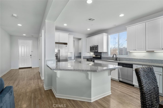 kitchen with a breakfast bar, sink, appliances with stainless steel finishes, light stone countertops, and white cabinets