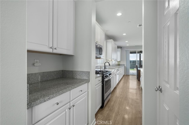 kitchen featuring white cabinetry, stainless steel appliances, light hardwood / wood-style floors, and dark stone counters