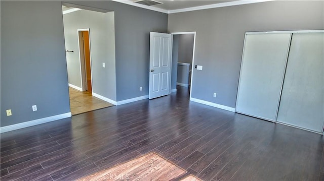 unfurnished bedroom with dark wood-type flooring, crown molding, and a closet