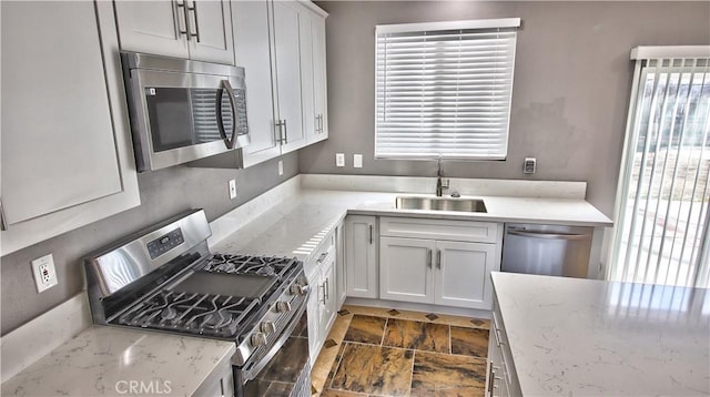 kitchen featuring stainless steel appliances, white cabinetry, light stone countertops, and sink