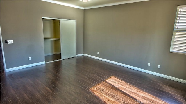 unfurnished bedroom with dark wood-type flooring, multiple windows, ornamental molding, and a closet