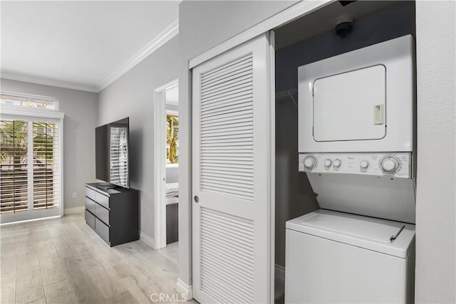 washroom featuring stacked washer / dryer, crown molding, and light hardwood / wood-style flooring