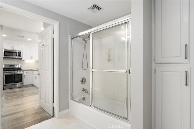 bathroom with tasteful backsplash, wood-type flooring, and combined bath / shower with glass door