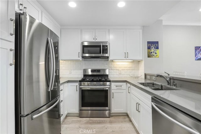 kitchen with sink, white cabinetry, tasteful backsplash, appliances with stainless steel finishes, and light hardwood / wood-style floors