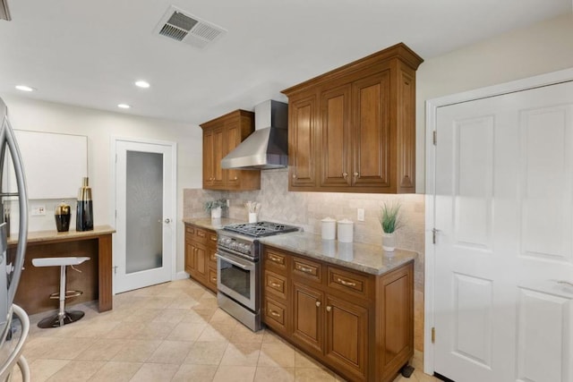 kitchen with light tile patterned floors, appliances with stainless steel finishes, light stone countertops, decorative backsplash, and wall chimney range hood