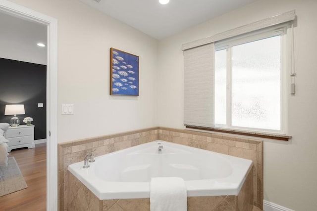 bathroom with plenty of natural light, tiled bath, and wood-type flooring