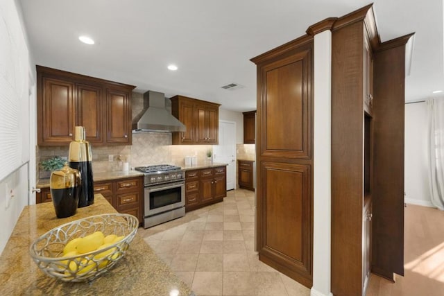 kitchen with backsplash, high end stainless steel range oven, wall chimney exhaust hood, and light stone countertops