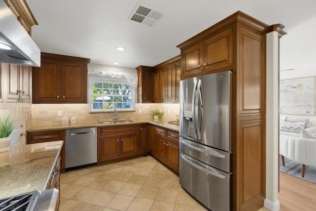 kitchen featuring wall chimney range hood, light stone countertops, sink, and appliances with stainless steel finishes