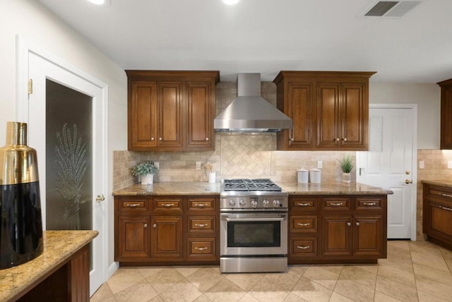 kitchen with wall chimney range hood, light tile patterned floors, stainless steel range, light stone countertops, and decorative backsplash