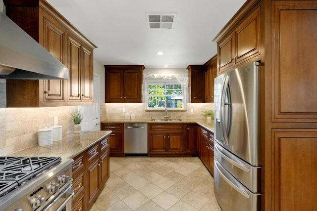 kitchen featuring tasteful backsplash, sink, light stone counters, stainless steel appliances, and wall chimney exhaust hood