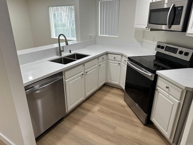 kitchen with appliances with stainless steel finishes, white cabinetry, sink, kitchen peninsula, and light wood-type flooring