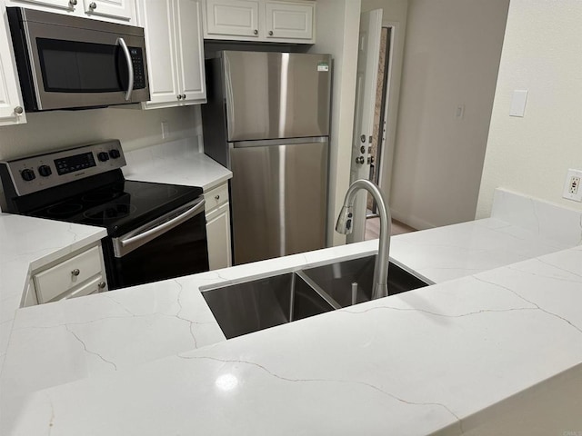 kitchen with light stone counters, white cabinetry, appliances with stainless steel finishes, and sink