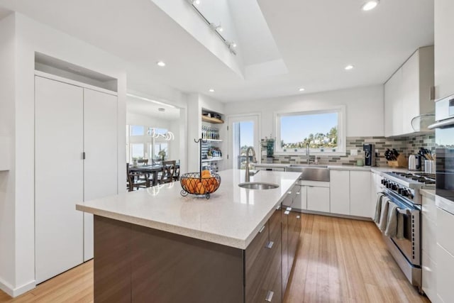 kitchen with white cabinetry, sink, stainless steel stove, and a center island with sink