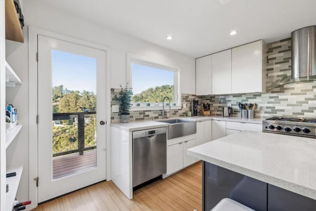 kitchen featuring sink, white cabinets, stainless steel appliances, wall chimney range hood, and light wood-type flooring