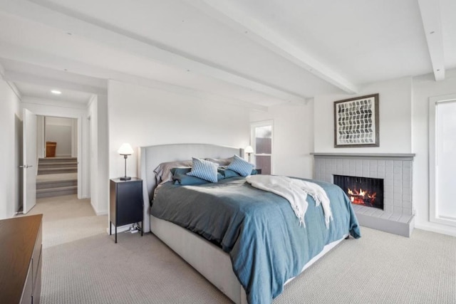 bedroom with a brick fireplace, beam ceiling, and light colored carpet