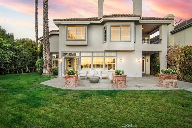 back house at dusk featuring a patio area, an outdoor hangout area, a balcony, and a lawn