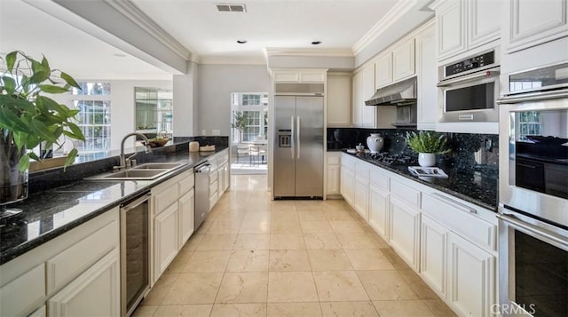 kitchen featuring sink, beverage cooler, dark stone counters, stainless steel appliances, and crown molding