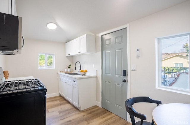 kitchen featuring sink, light wood-type flooring, white cabinets, and black gas stove