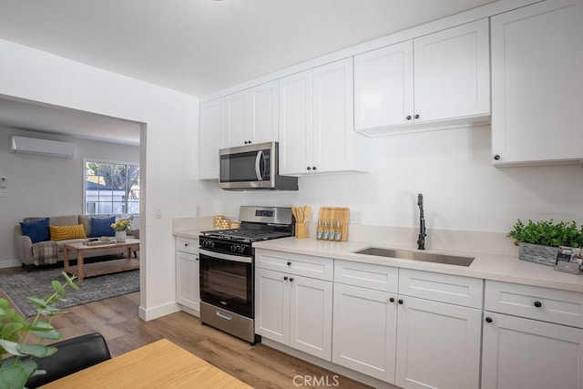 kitchen with sink, white cabinetry, a wall mounted AC, appliances with stainless steel finishes, and light hardwood / wood-style floors