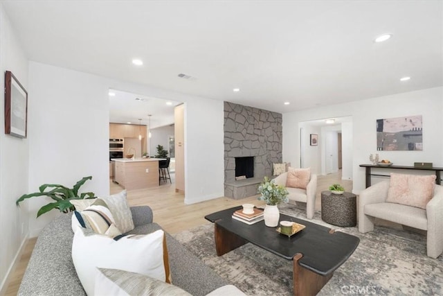 living room with a stone fireplace and light wood-type flooring