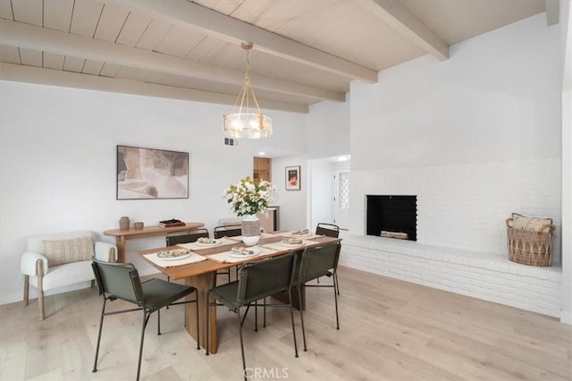 dining space with beam ceiling, wood ceiling, a fireplace, and light hardwood / wood-style flooring