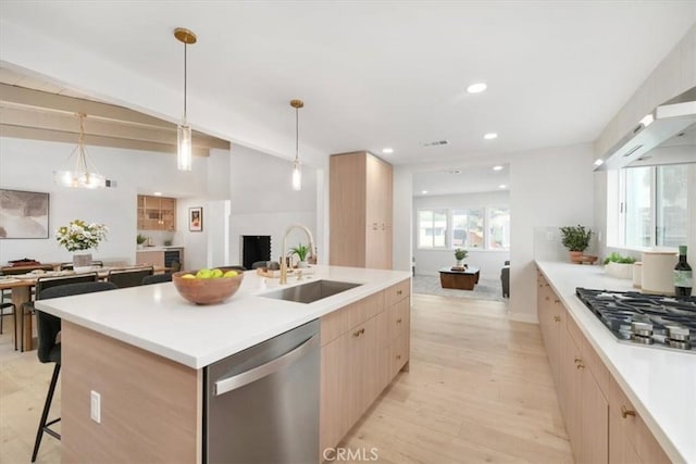 kitchen with decorative light fixtures, sink, a kitchen island with sink, stainless steel appliances, and light wood-type flooring