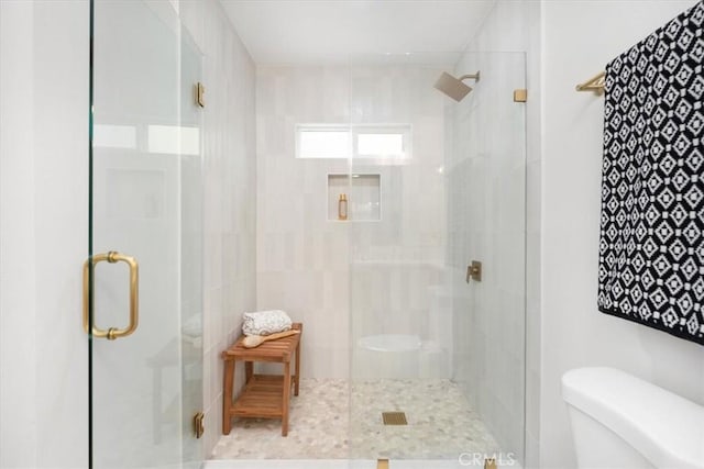 bathroom featuring a shower with door and toilet