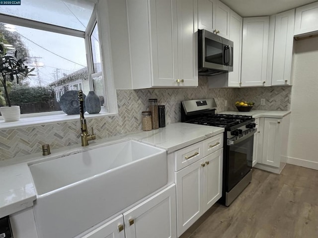 kitchen with sink, appliances with stainless steel finishes, white cabinetry, light stone counters, and tasteful backsplash