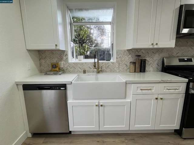 kitchen with white cabinetry, sink, backsplash, stainless steel appliances, and light stone countertops