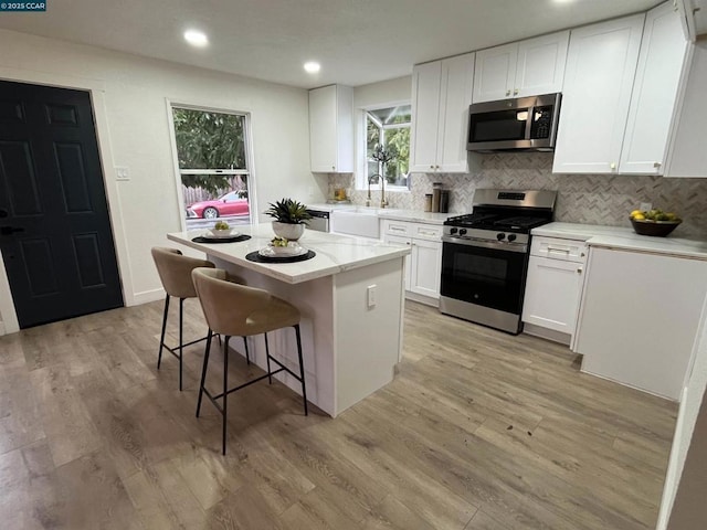 kitchen with sink, appliances with stainless steel finishes, white cabinets, a kitchen island, and decorative backsplash