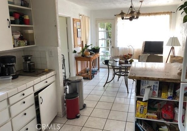 kitchen featuring an inviting chandelier, light tile patterned floors, tile counters, white cabinets, and backsplash