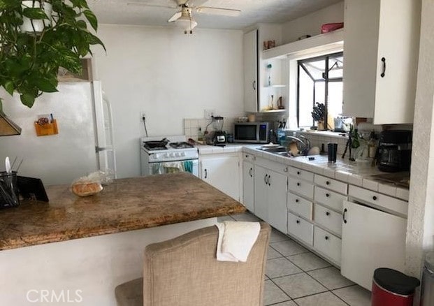 kitchen featuring light tile patterned floors, white appliances, ceiling fan, white cabinetry, and tile counters