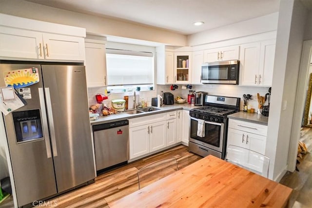 kitchen with sink, white cabinetry, tasteful backsplash, light wood-type flooring, and stainless steel appliances