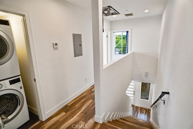 laundry area with stacked washer / drying machine, electric panel, and wood-type flooring