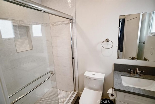 bathroom featuring a shower with door, vanity, and toilet