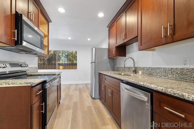 kitchen with light hardwood / wood-style floors, appliances with stainless steel finishes, light stone countertops, and sink