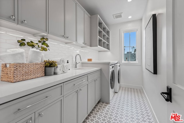 clothes washing area with cabinets, washing machine and clothes dryer, and sink