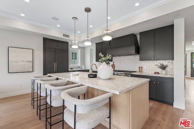 kitchen with pendant lighting, an island with sink, a kitchen bar, custom exhaust hood, and ornamental molding