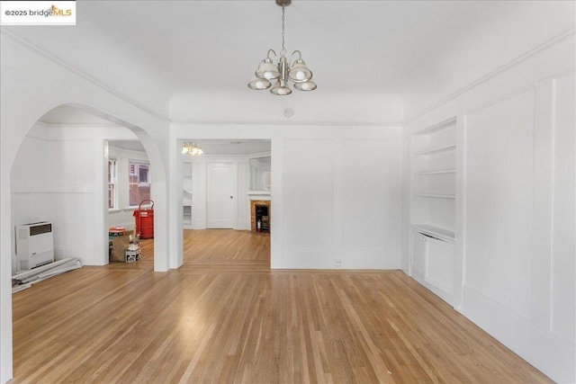 empty room featuring an inviting chandelier, hardwood / wood-style flooring, heating unit, and built in features